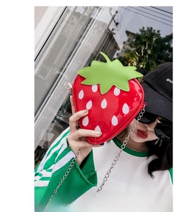 Detail of red strawberry-shaped crossbody bag with white dots and green leaf trim