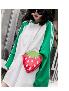 Detail of creative strawberry crossbody bag featuring glossy red finish and leaf texture