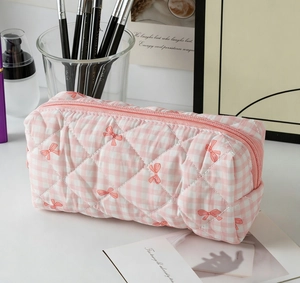 Detail of pink plaid quilted makeup bag with red bow prints and a sturdy metal zipper