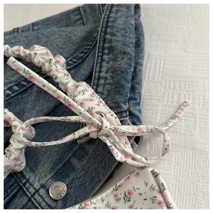 Detail of floral fabric accessory with pink patterns and metal grommet on denim background