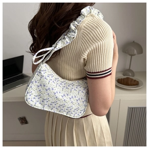 Floral shoulder bag with ruffled strap shown on shoulder in a warm minimalist setting