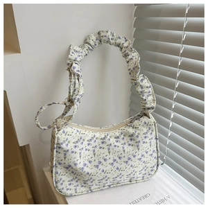 Detail of floral print handbag featuring cream fabric with purple flowers and ruched handle