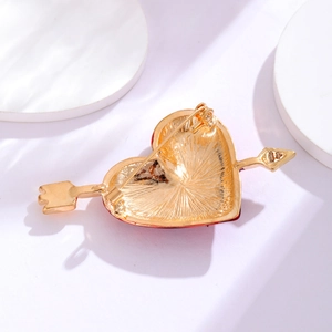 Arrow through heart brooch with red enamel and gold metal backing on white stand