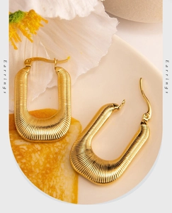 Close-up of golden U-shaped earrings with fine horizontal ribbed texture on a white tray