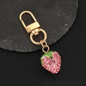 Close-up of a pink rhinestone strawberry keychain on a stone with gold metal clasp