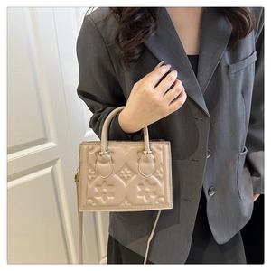 Detail of embossed floral patterns on the beige crossbody bag with top handle