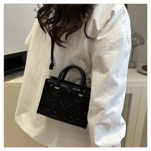 Detailed close-up of a black embossed square bag with gold hardware and a shoulder strap