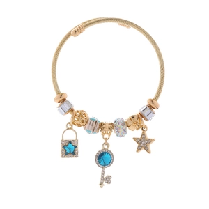 Dettaglio di un bracciale dorato con ciondoli a stella e chiave in cristallo blu e bianco