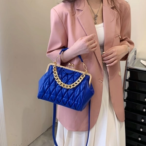 Blue quilted crossbody bag with gold chain and vintage frame closure on pink suit