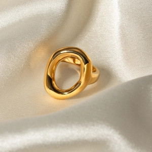 Polished 18k gold plated stainless steel hollow oval ring on elegant champagne silk fabric