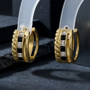 Macro shot of gold hoop earrings with black and clear zircons on grey stone background