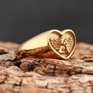Détail macro d'une bague chevalière cœur avec ange doré sur fond bois naturel