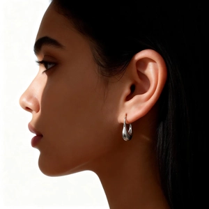 Macro side view of polished silver water drop earrings on model with artistic lighting