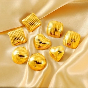 Macro detail of gold titanium steel earrings featuring brushed metal texture on silk