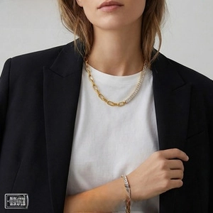 Detail of a gold tennis chain necklace and bracelet set worn over a black blazer