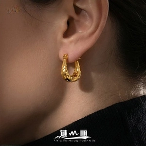 Close-up of chunky gold U-shaped earrings with hammered texture on a model's ear