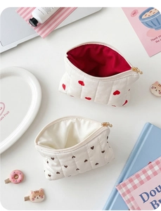 Flat lay of quilted cotton heart pattern pouches with golden zippers on white surface