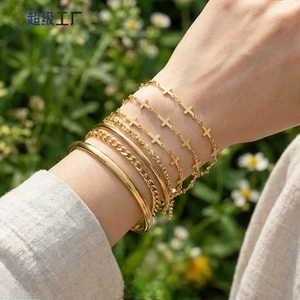 Close-up of gold layered bracelet set with cross pendant and open bangle in sunlight