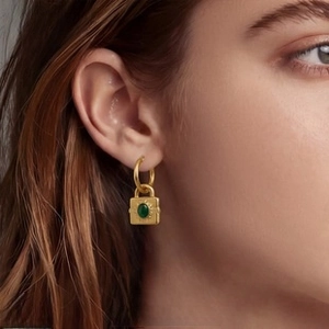Close-up of gold drop earring with a square lock pendant featuring a green gemstone