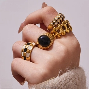 Detail of four gold rings featuring black enamel checks and braided textures on hand