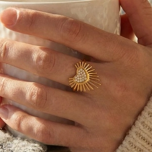Detail of a 18K gold heart-shaped ring with pavé zircons and sunburst rays on a model's hand