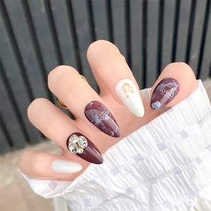 Close-up of long almond press-on nails with burgundy finish, rhinestones, and pearls