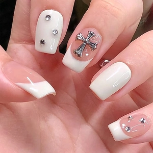 Detail of French white press-on nails with silver gothic cross and rhinestone accents
