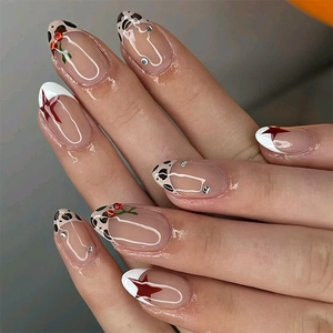 Macro view of French tip nails with cow print, cherry charms, and red star details