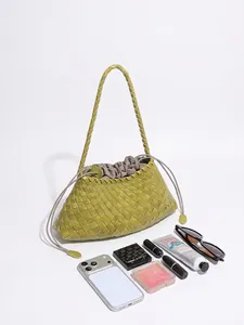 Handwoven green leather tote bag with drawstring closure and shoulder strap shown with essentials