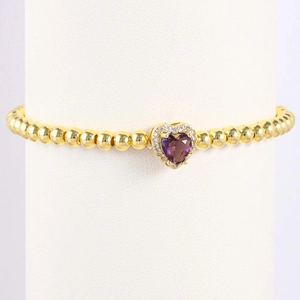 Close-up of gold beaded bracelet featuring a purple heart-shaped stone pendant with crystals
