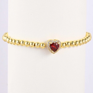 Macro view of gold beaded bracelet featuring a heart-shaped red gemstone and pavé stones