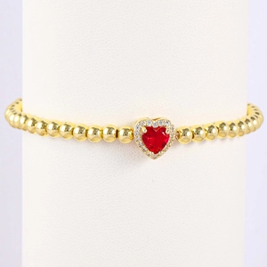 Macro detail of gold beaded bracelet featuring a red heart gemstone and white zircon halo