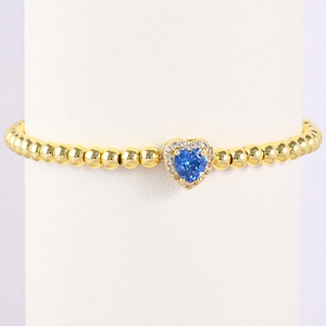 Detail of gold beaded bracelet with blue heart gemstone and white zircon halo