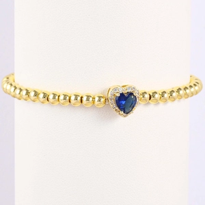 Close-up of golden beaded bracelet with a blue heart-shaped birthstone and crystals