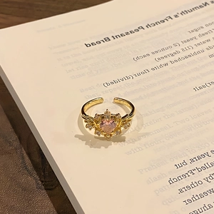 Detailed view of adjustable gold heart ring with pink gemstone on an open book