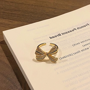 Detailed shot of a gold bow-shaped ring with pavé crystals on a white book surface