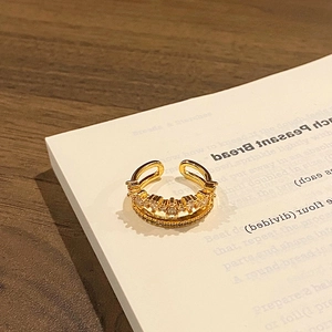 Detail of a gold-plated double-layer open ring with white zircon on a book page