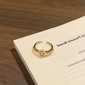 Macro detail of gold adjustable ring with central gemstone and tiny pearls on a book