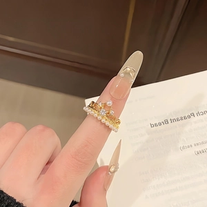 Close-up of a golden crown ring with white pearls and zircons worn on a finger
