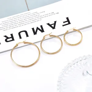 Three sizes of gold stainless steel hoop earrings with textured mesh pattern on magazine