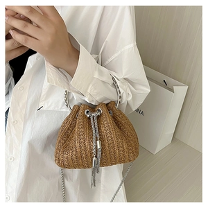 Close-up of woven straw bucket bag with silver metal handle and tassel details