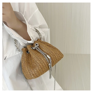 Detail of straw bucket bag with silver metal handle, drawstring closure and chain strap