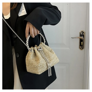 Detail of straw bucket bag with silver ring handle and shimmering metallic tassels