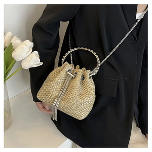 Detail view of woven straw bucket bag with metal ring handles and elegant tassel accents