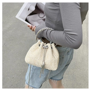 Detail of beige woven straw bucket bag with silver handles and chain strap in outdoor setting