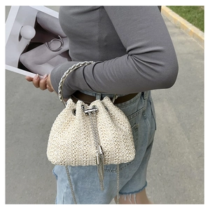 Detail of straw bucket bag with metal ring handle, tassel accents and chain strap