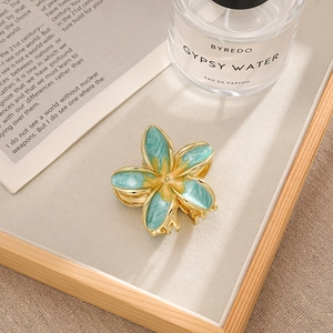 Detail view of a small blue and yellow plumeria hair claw clip on a wooden tray
