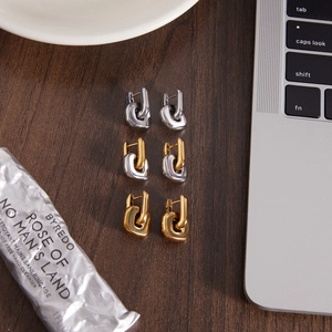 U-shaped chain link earrings in gold and silver finish on a wooden desk setting