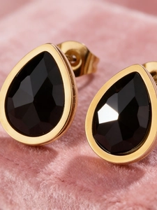 Macro-opname van 18k gouden druppeloorbellen met zwarte zirkoon op roze fluweel