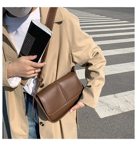 Detail of dark brown leather crossbody bag with white stitching and adjustable wide strap